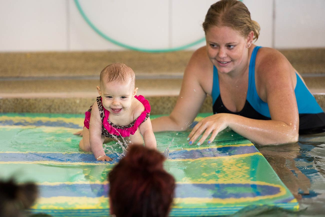 smiling baby crawling on floating mat in the water