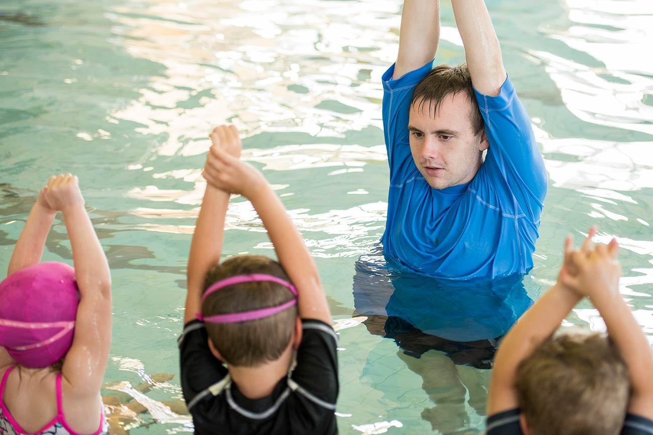 children with teacher preparing their arms to dive